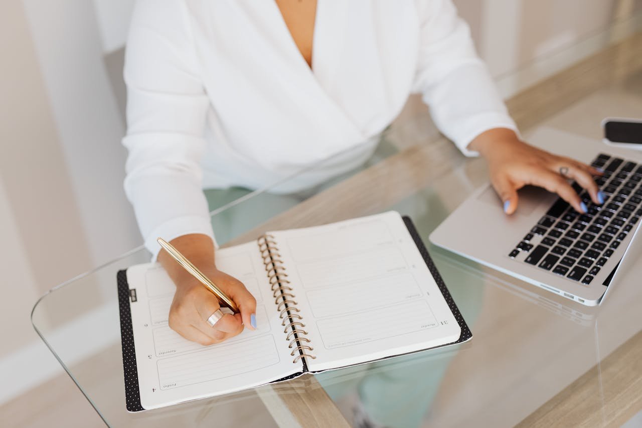 A person planning and typing on a laptop at a glass desk.